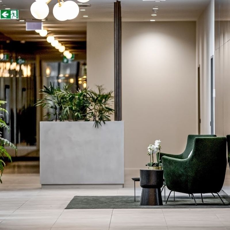 Modern BTR lobby with green chair, marble desk, white planter with plants, and decorative lamps.