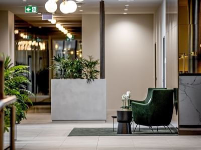 Modern BTR lobby with green chair, marble desk, white planter with plants, and decorative lamps.