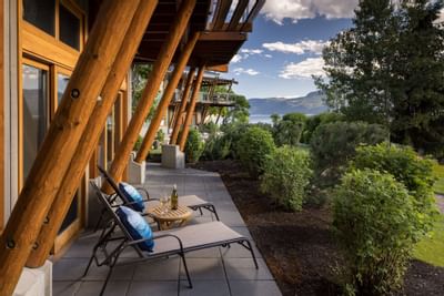 Outdoor patio with two lounge chairs, a small table, and a view of mountains and water.