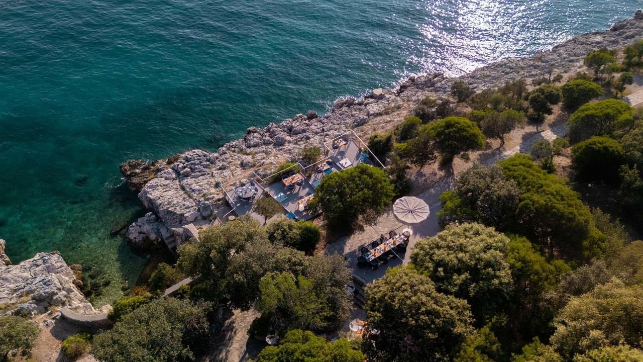 Vista aerea di una spiaggia rocciosa con un ristorante e una piscina all'aperto.