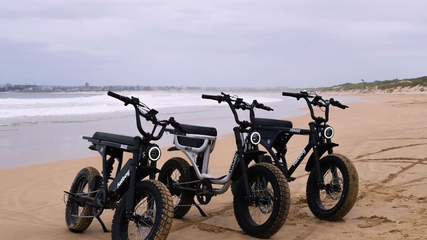 Three electric bikes parked on a beach by the ocean, with tracks in the sand surrounding them near the Mauad Hotel