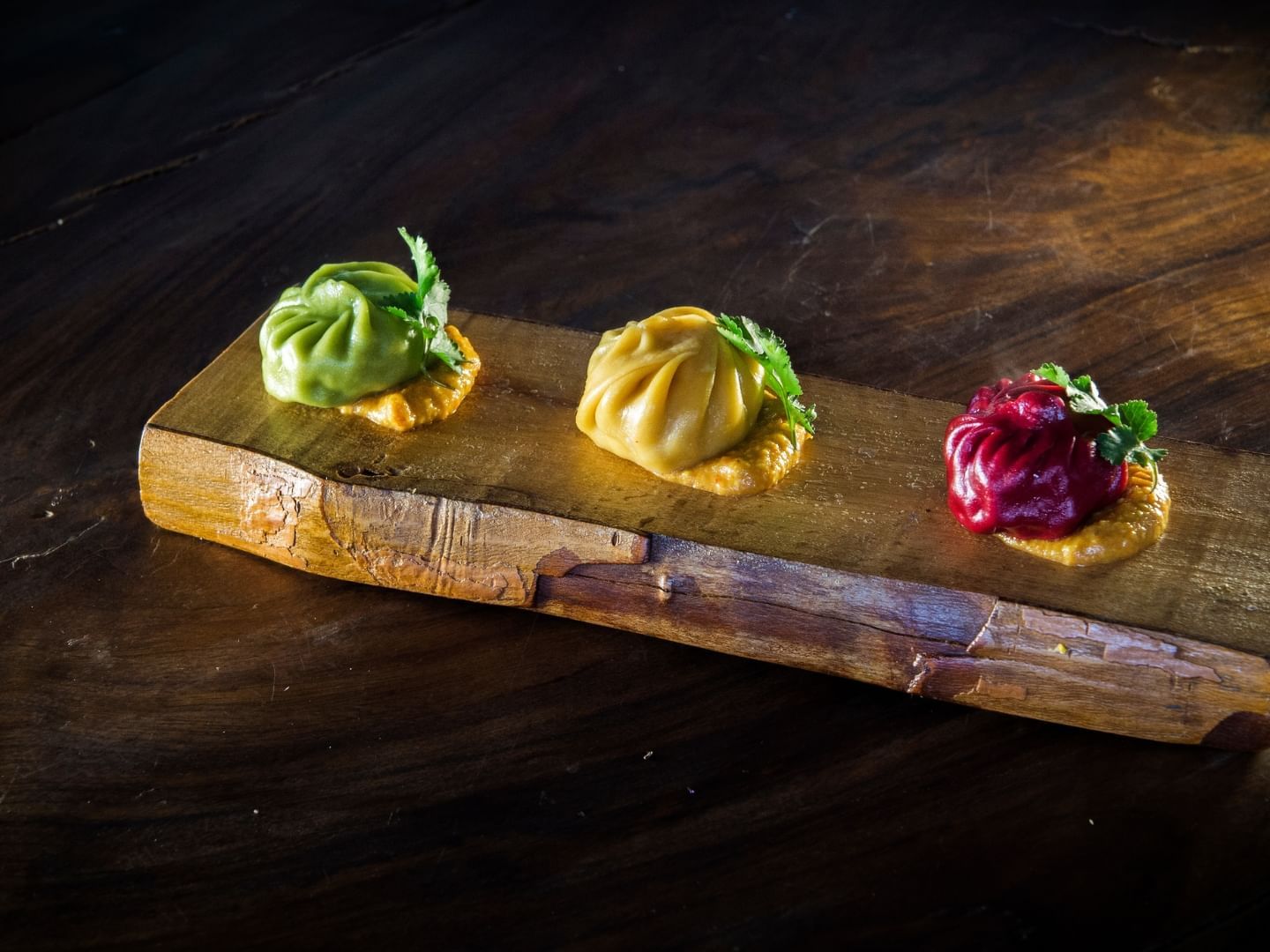 Three colorful dumplings garnished with cilantro on a wooden board with sauce at Dwarika's Himalayan Wellbeing