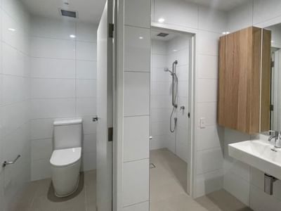 Clean bathroom with white tiles, toilet, shower, and sink within a 4 Bedroom Twin Share Apartment at UniLodge Brisbane City.
