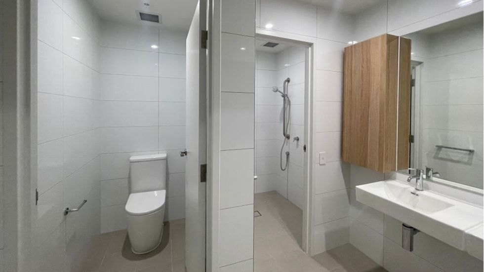 Clean bathroom with white tiles, toilet, shower, and sink within a 4 Bedroom Twin Share Apartment at UniLodge Brisbane City.