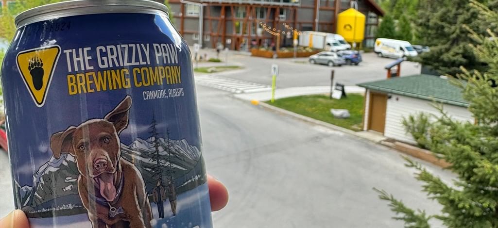 Someone holds up a can of beer from The Grizzly Paw Brewing Company in Canmore from a patio.
