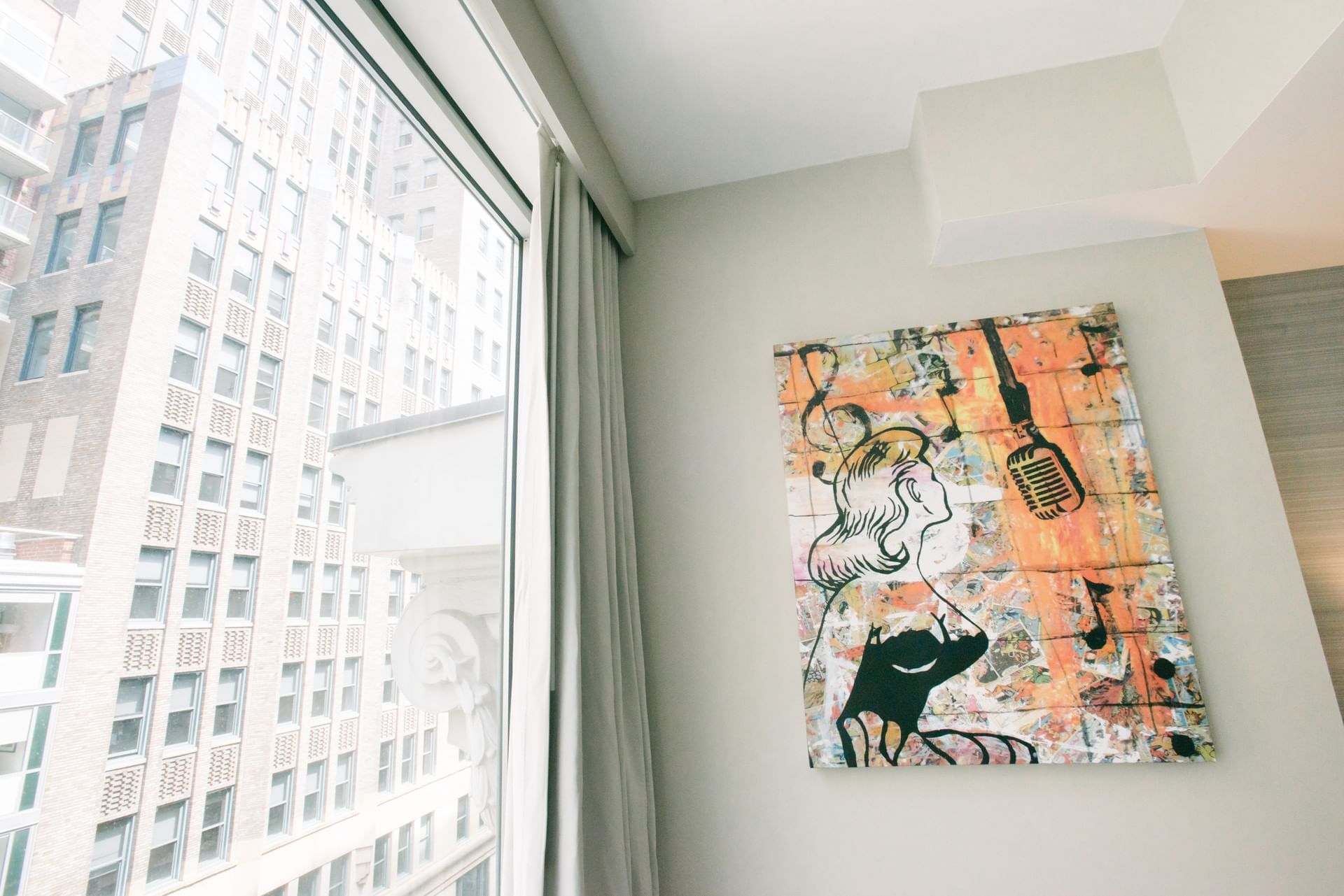A room with a large window showing a city view and a piece of artwork on the wall