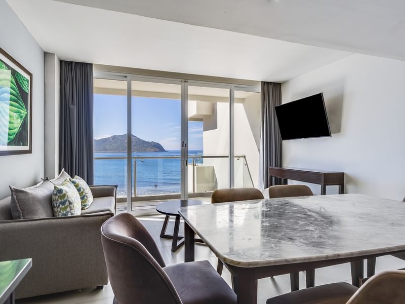 Luxury Suite living area featuring a dining table, a cozy sofa, a TV, and a scenic view of the bay at Sunvivia Mazatlán