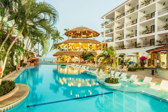 Bright blue swimming pool beside white multistory buildings facing a colonial-style architecture at Los Arcos Suites