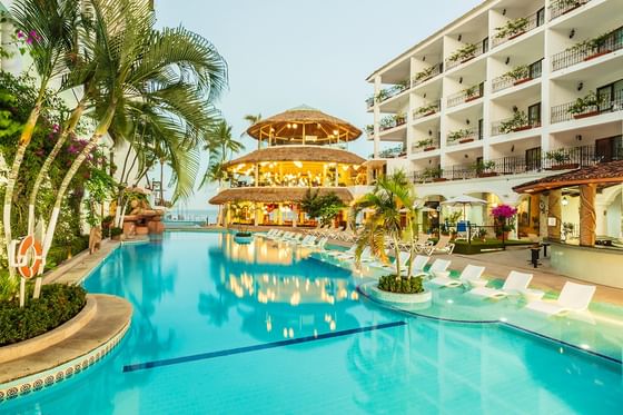 Bright blue swimming pool beside white multistory buildings facing a colonial-style architecture at Los Arcos Suites