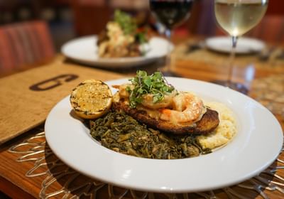 Gourmet shrimp and grits served with greens, grilled lemon, and wine in Cora's Restaurant at The White House Hotel