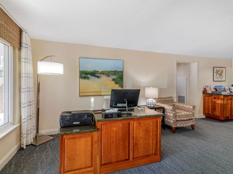 A hotel lobby work area with a desk, chair, computer, printer, and painting.