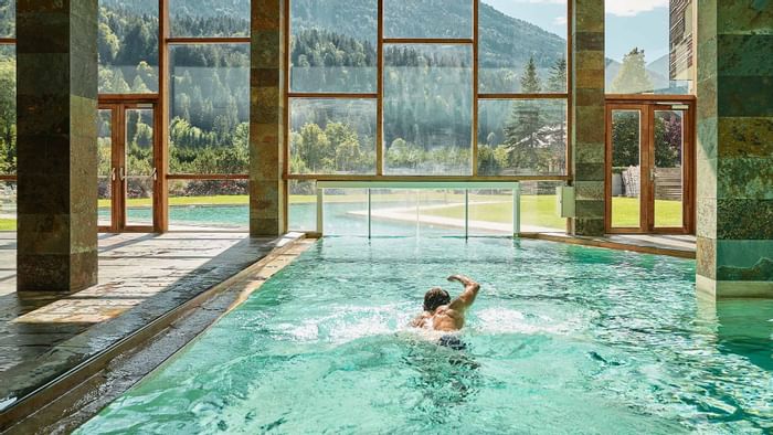 A man swimming in the indoor pool with mountain view at Falkensteiner Hotels & Residences