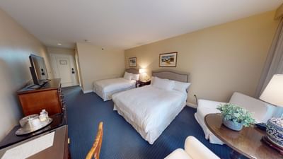 Two queen beds near armchairs and a glass-top table with a plant in the guest room at Avon Old Farms Hotel