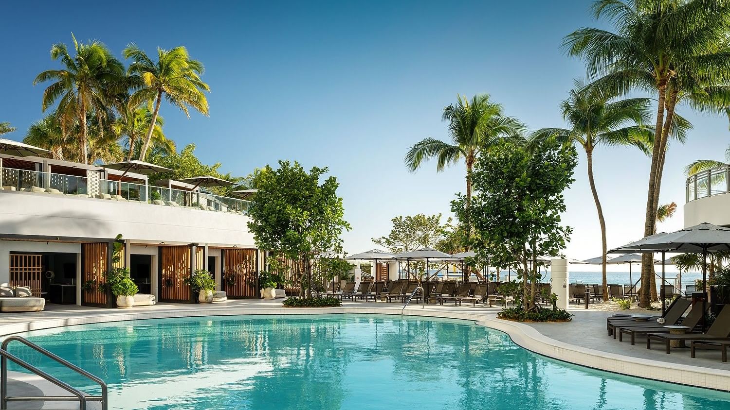 Tropical lagoon pool deck with resort loungers, cabanas, and palm-lined pathways.