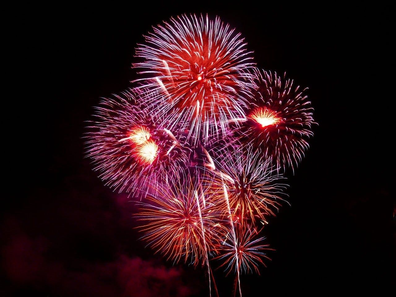 Red and orange fireworks explode at night on July 4th.