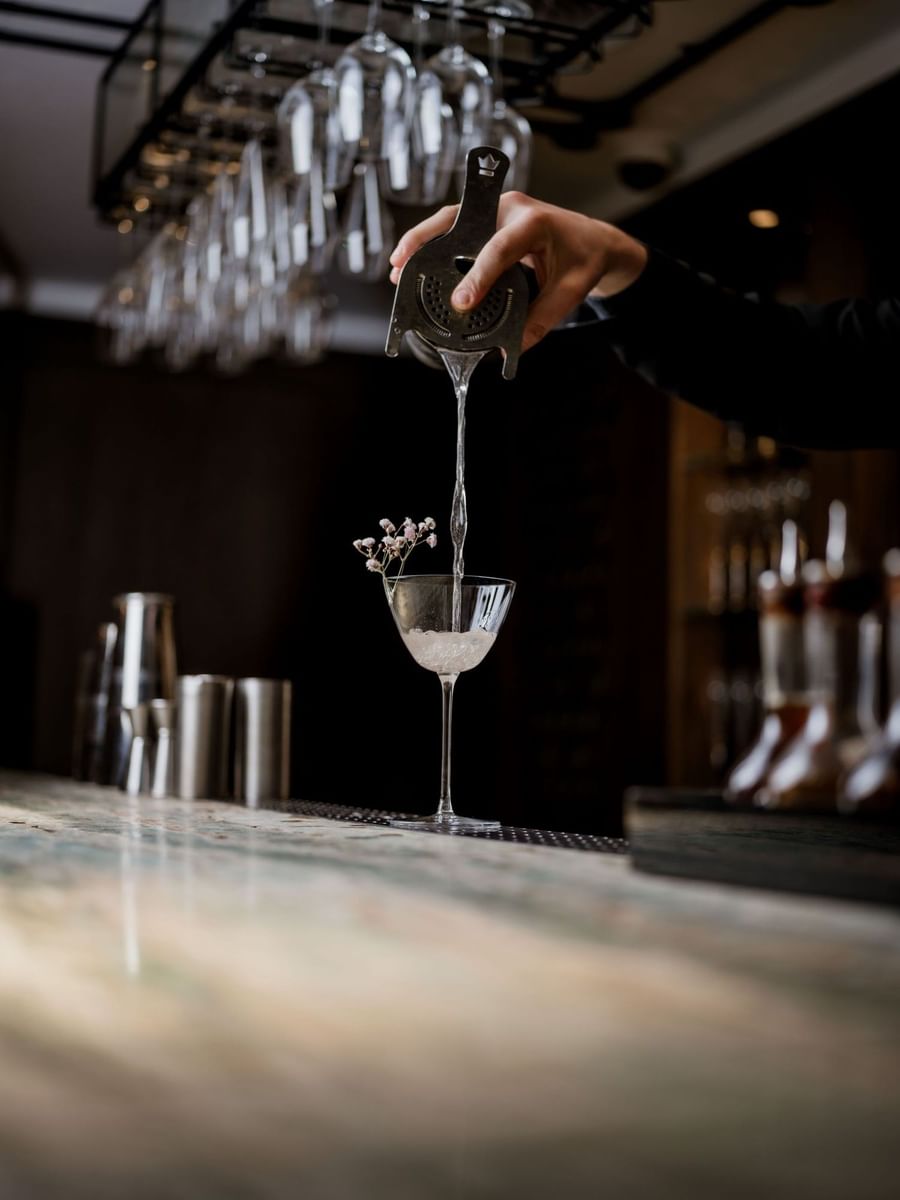Bartender straining a cocktail into a glass garnished with dried flowers at May Fair Kitchen