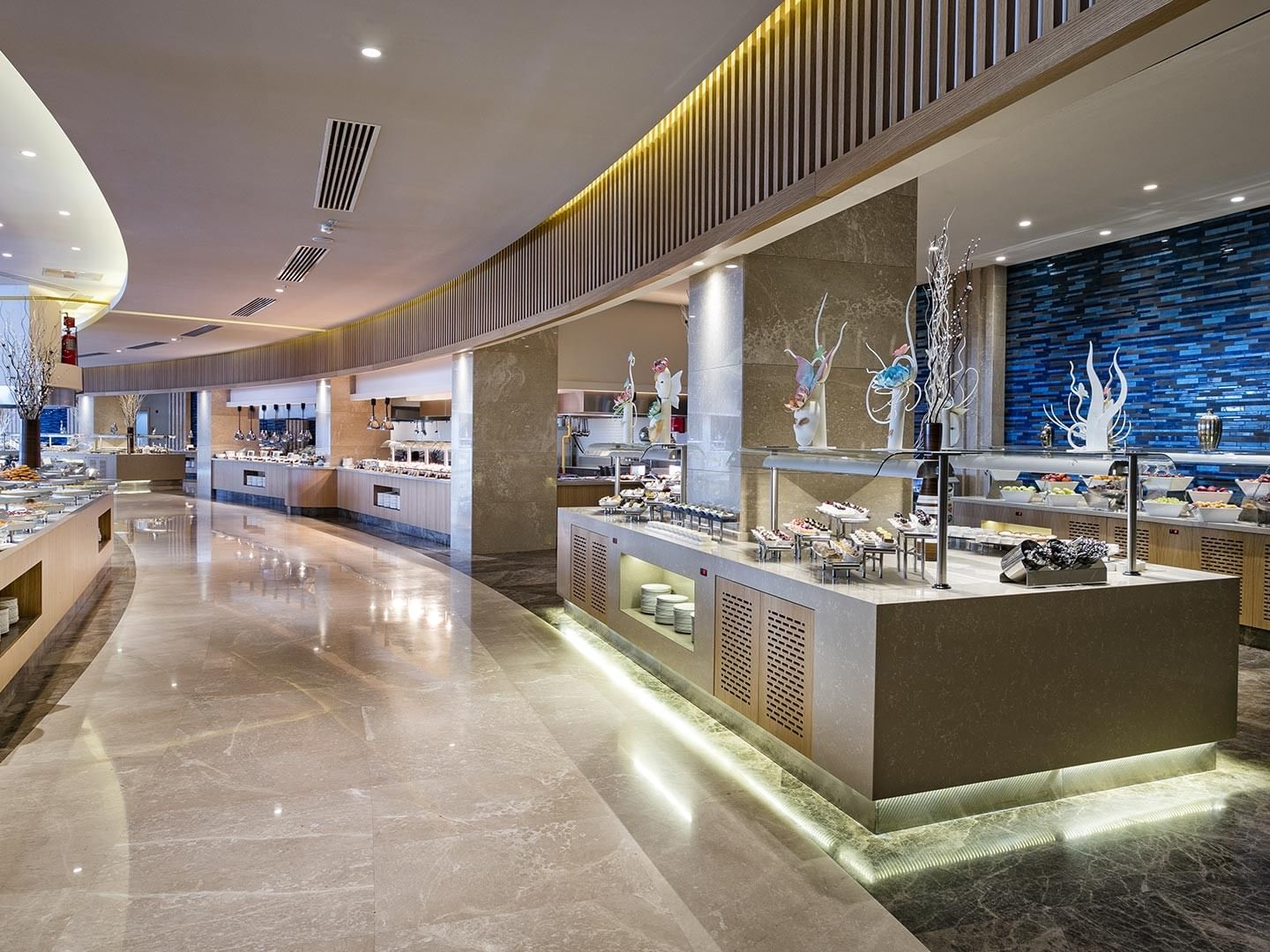 Spacious blue-walled restaurant with long counters and rich food displays at Titanic Luxury Collection Bodrum.