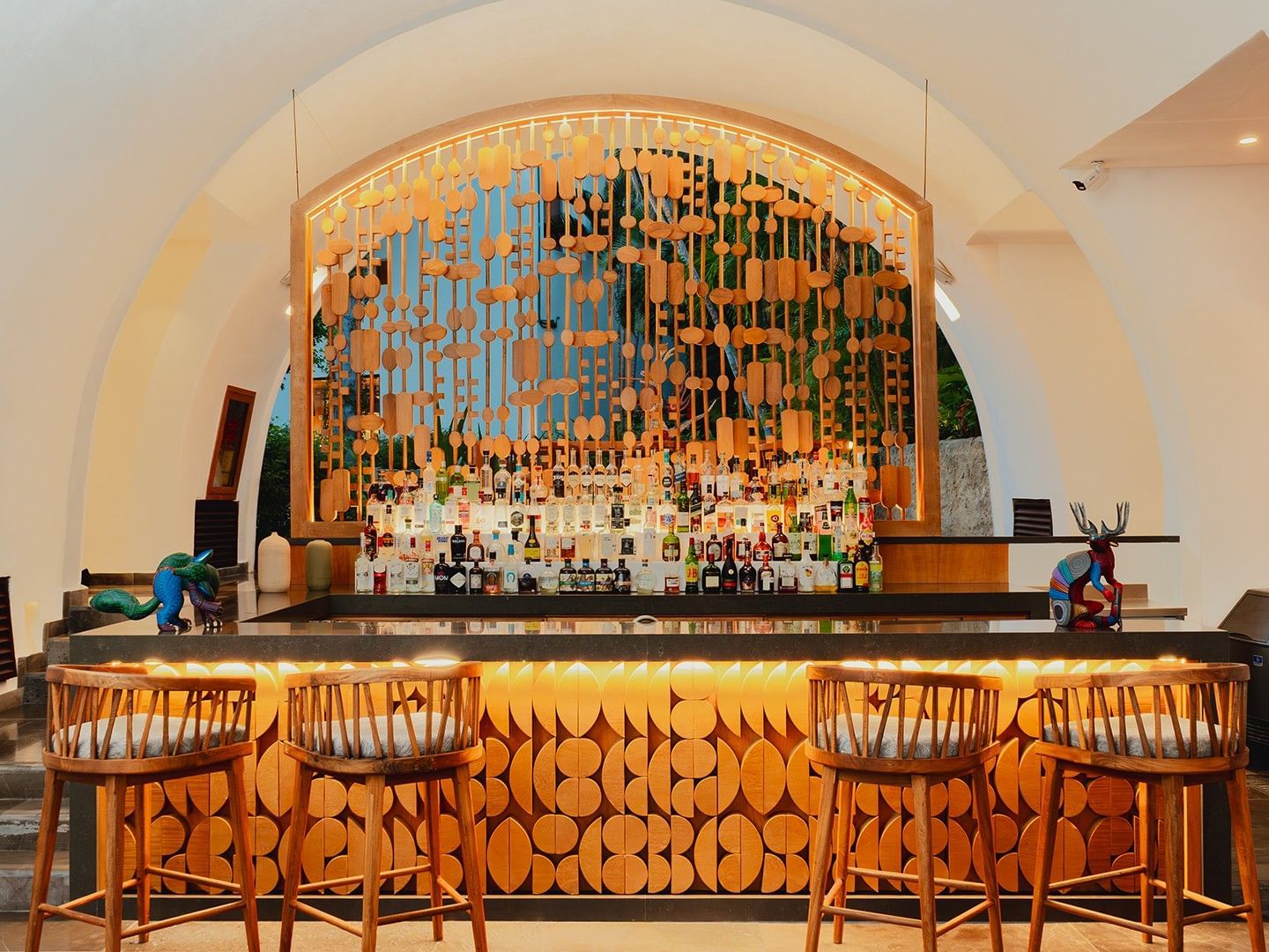 Bar counter with a carved wood facade and illuminated bottle shelf in Bitza Lounge Bar at Camino Real Zaashila Huatulco