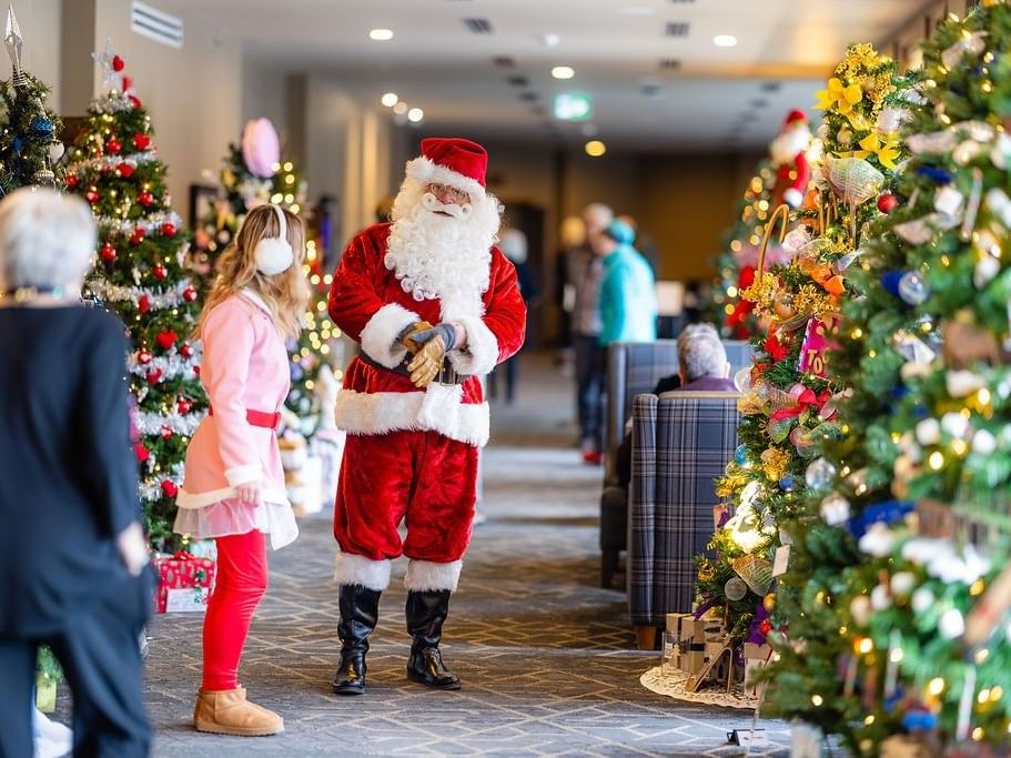 Festive holiday scene at Spring Creek Resorts with Santa and an elf standing among decorated Christmas trees