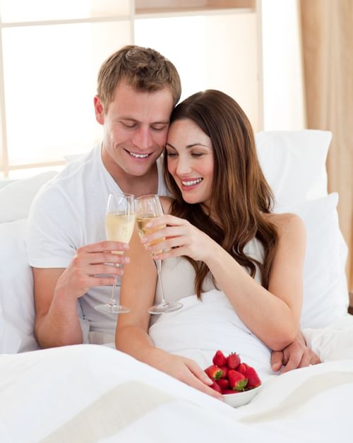 couple drinking wine and eating strawberries in bed