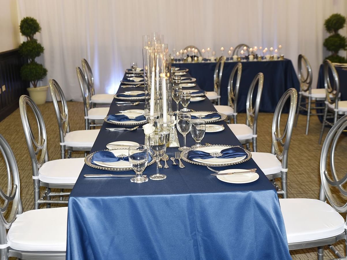 A long table with a blue cloth and silver chairs set for an event in the Blue Mahoe Suite at Courtleigh Hotel & Suites