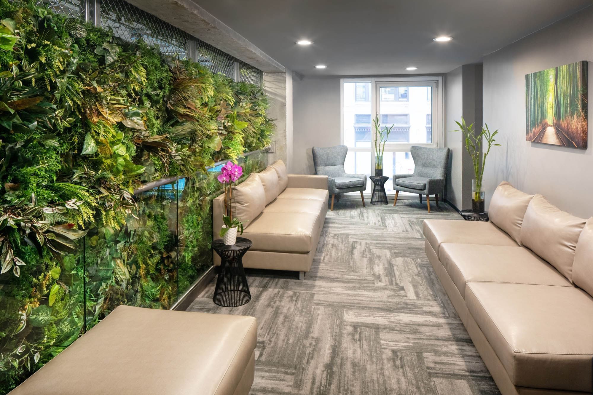 A lobby with a large green plant wall, beige couches, and gray chairs.