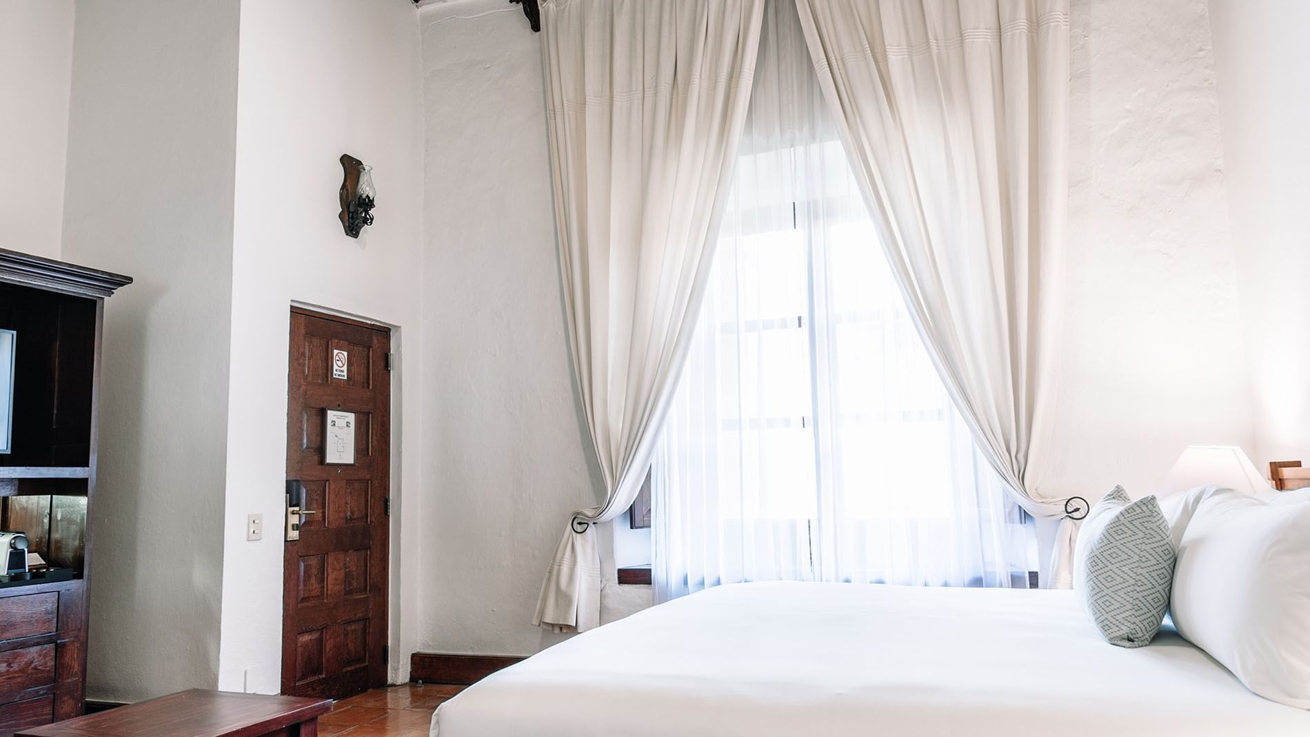 Bright, airy bedroom with white walls and curtains in the King Governor Suite at Quinta Real Oaxaca