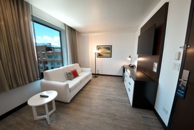 Living area on a room with couch, TV, floor lamp and window with city view at D Sabana Hotel, San Jose Costa Rica Hotel