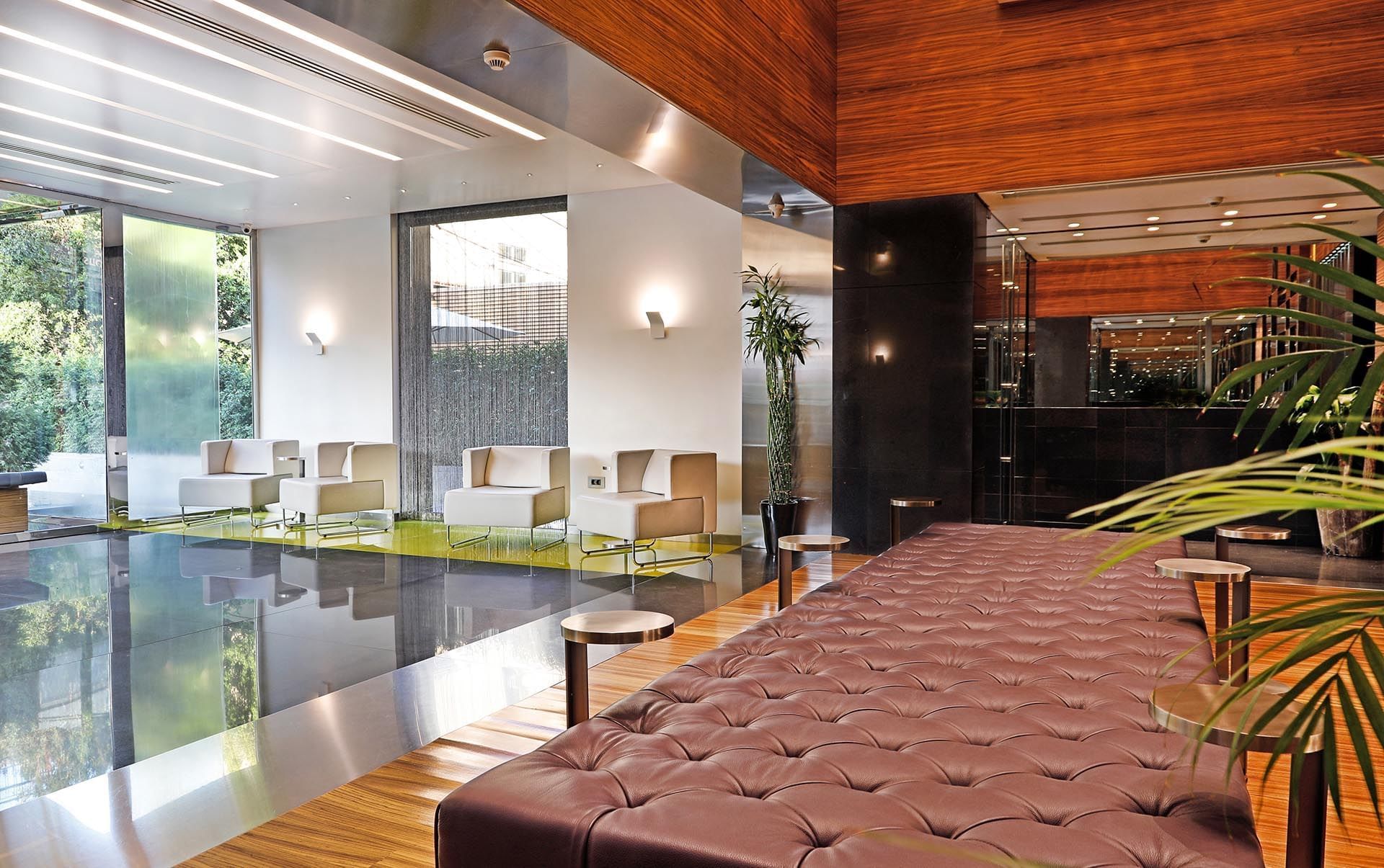 Tufted leather bench by metal tables near white armchairs under a wood ceiling at Warwick Stone 55 - Beirut