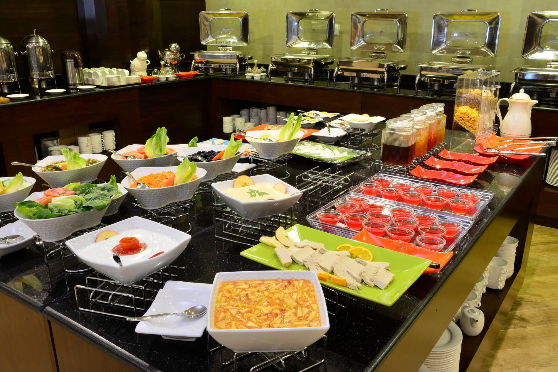 Fresh salads & desserts in white bowls by metal food warmers served in Naviti Restaurant at Naviti By Warwick Dammam buffet