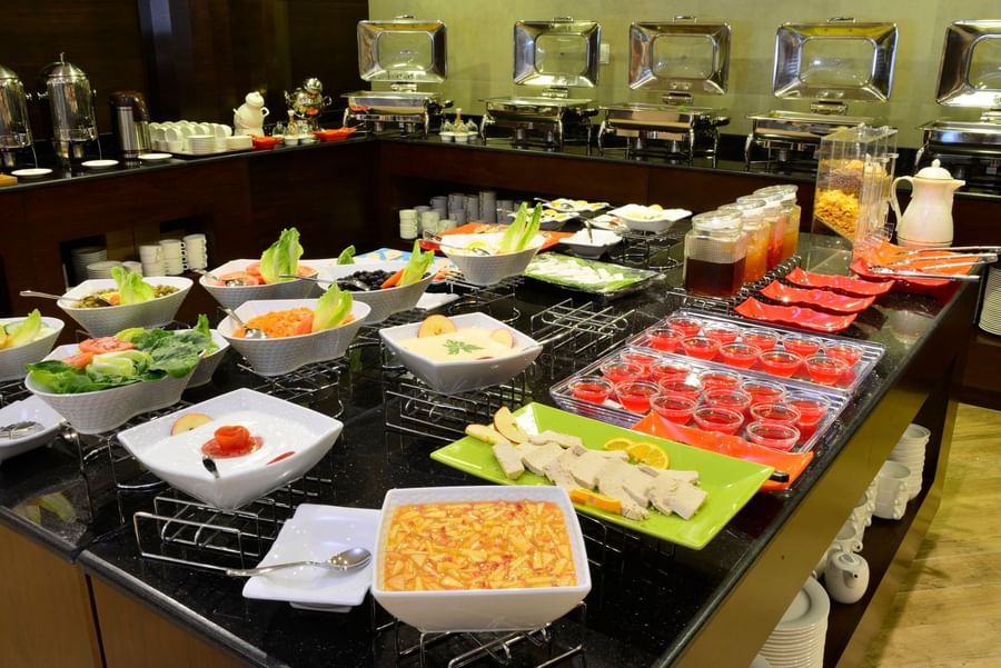 Fresh salads and desserts in white bowls by metal food warmers at Naviti By Warwick Dammam buffet