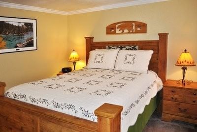 Studio Suite​ with a queen bed, wooden headboard, rustic quilt, and bear carving wall decor at Americana Village Suites