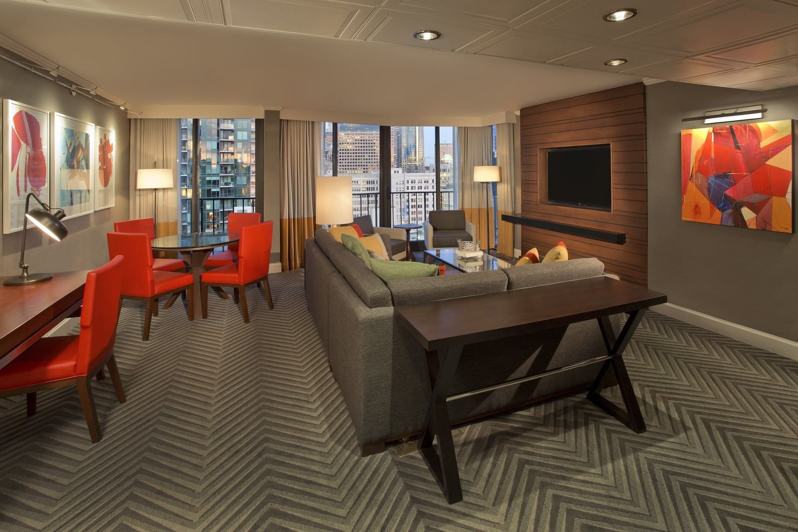 A wide view of a hotel suite with a living room, dining area, and city view.