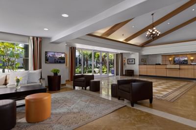 Lobby with a gray sofa by a dark coffee table and ottomans at Anaheim Portofino Inn & Suites