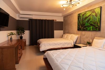 Two beds facing TV and wooden dresser in Deluxe Double at MARINN Tropical Vibes Hotel