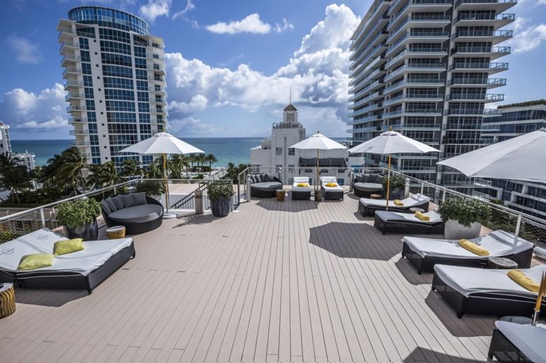 A rooftop pool deck with lounge chairs, umbrellas, and a city view