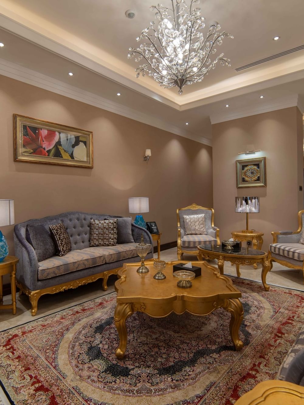 Tufted gray sofas by gold-carved coffee tables on a traditional Persian rug in Penthouse Villa at Warwick Al Khobar