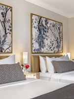 Bed with a side table under hanging pattern wall art in Executive Two Queen Beds at Warwick Allerton Chicago