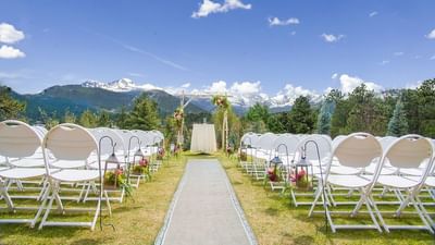 An outdoor wedding ceremony with white chairs and floral lanterns leading to an archway against a mountain backdrop