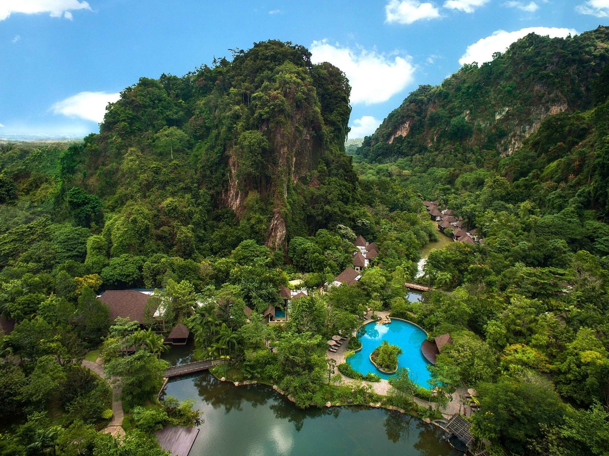 Aerial view of The Banjaran Hotsprings Retreat featuring elegant lodges, a blue swimming pool, and a tranquil pond
