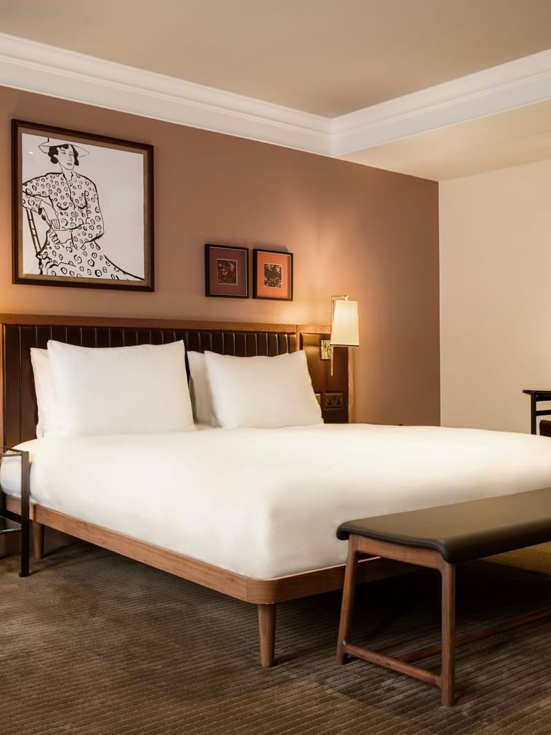 Collection Superior Room with two white pillows, a large king bed, and a bench at The May Fair Hotel, London.