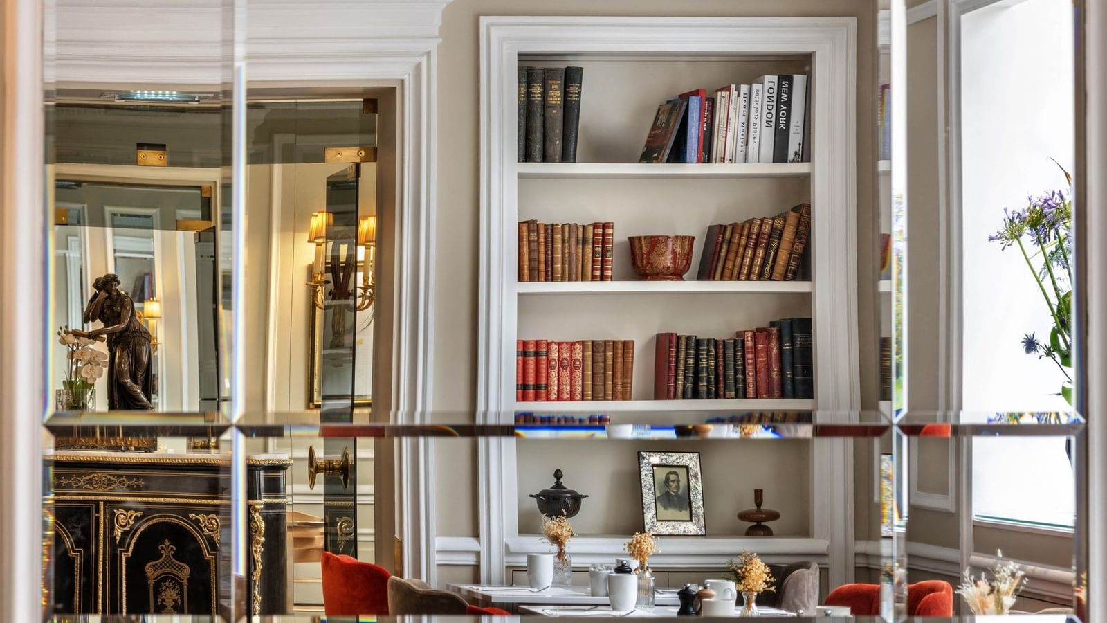 Dining table with white tableware placed by a bookshelf with antique books and gold-framed art at Hotel Westminster Paris