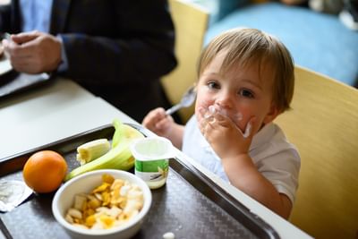 Happy baby toddler eating breakfast from a tray with yogurt, fruit, and cereal bowl at Rodd Moncton hotel dining room