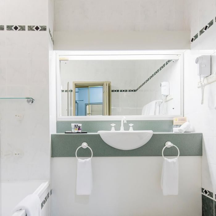 Interior of a white tiled bathroom with a bathtub and vanity with illuminating mirror at Mercure Charlestown