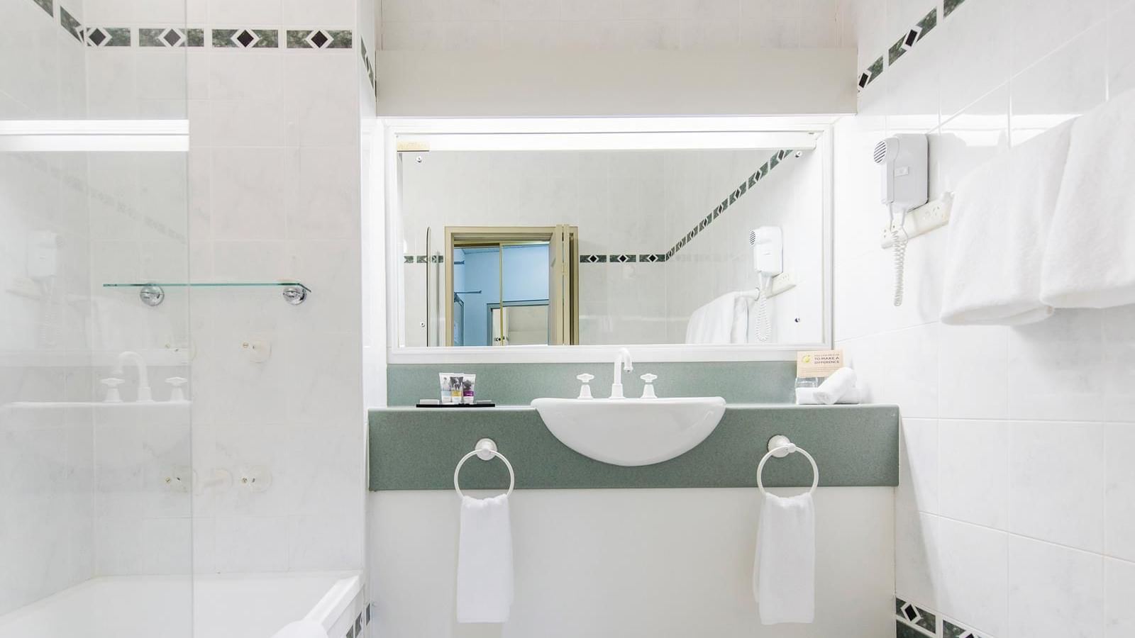 Interior of a white tiled bathroom with a bathtub and vanity with illuminating mirror at Mercure Charlestown