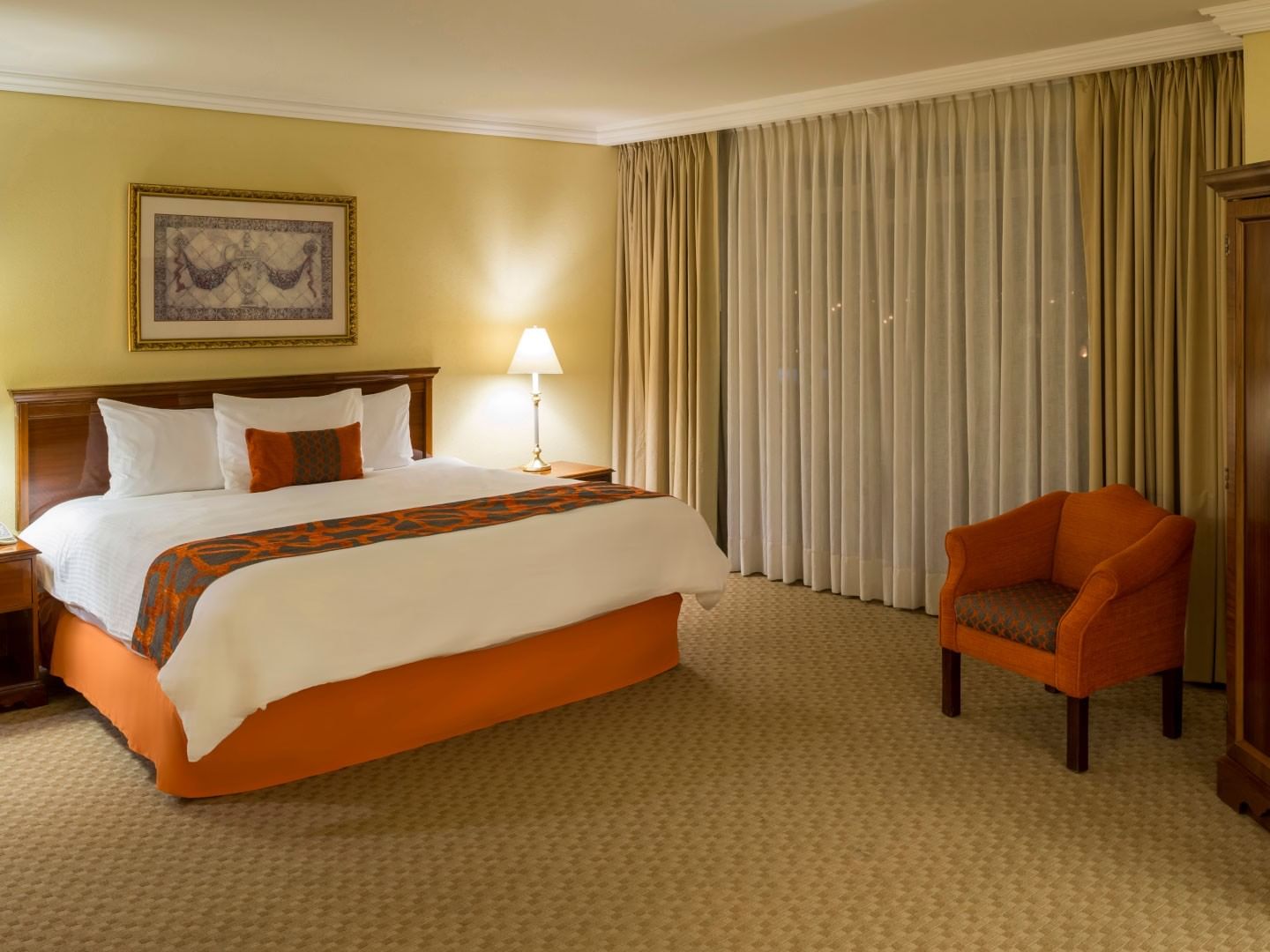 Junior Suite King con cama king, sillón naranja y muebles de madera en Camino Real Puebla Angelópolis