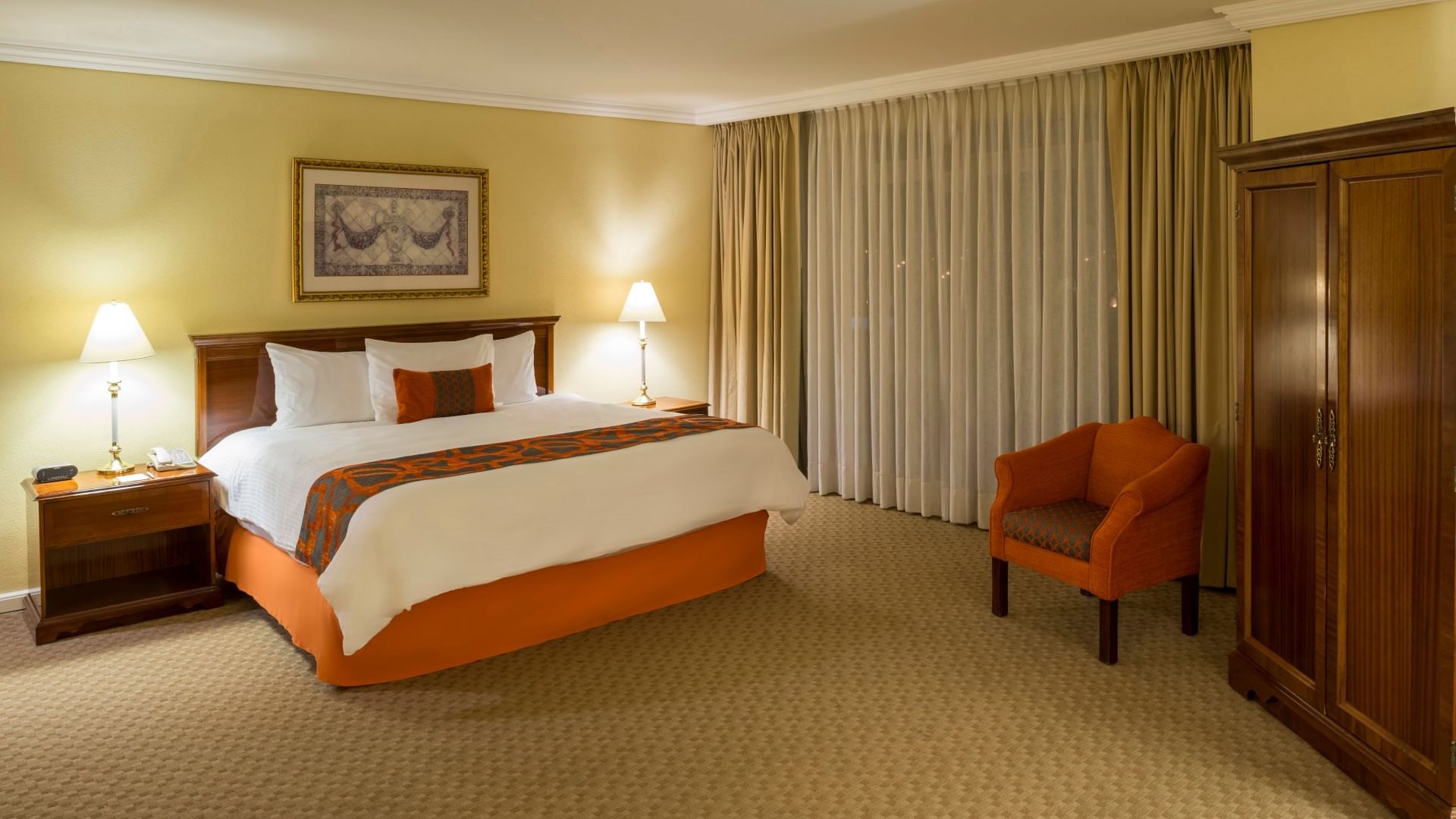 Junior Suite King con cama king, sillón naranja y muebles de madera en Camino Real Puebla Angelópolis