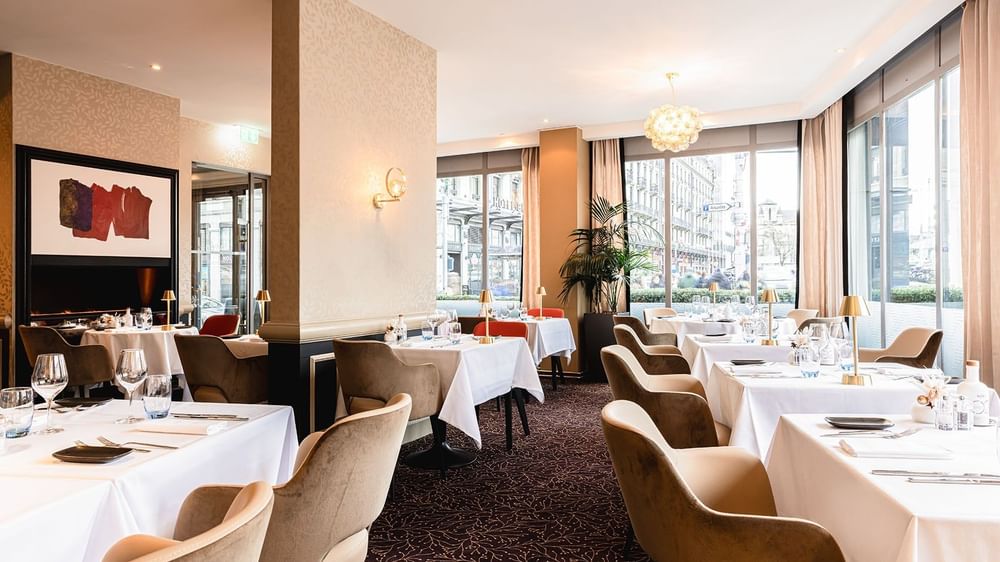 Plush armchairs surrounding white linen tables by bright city windows in Téséo at Warwick Geneva