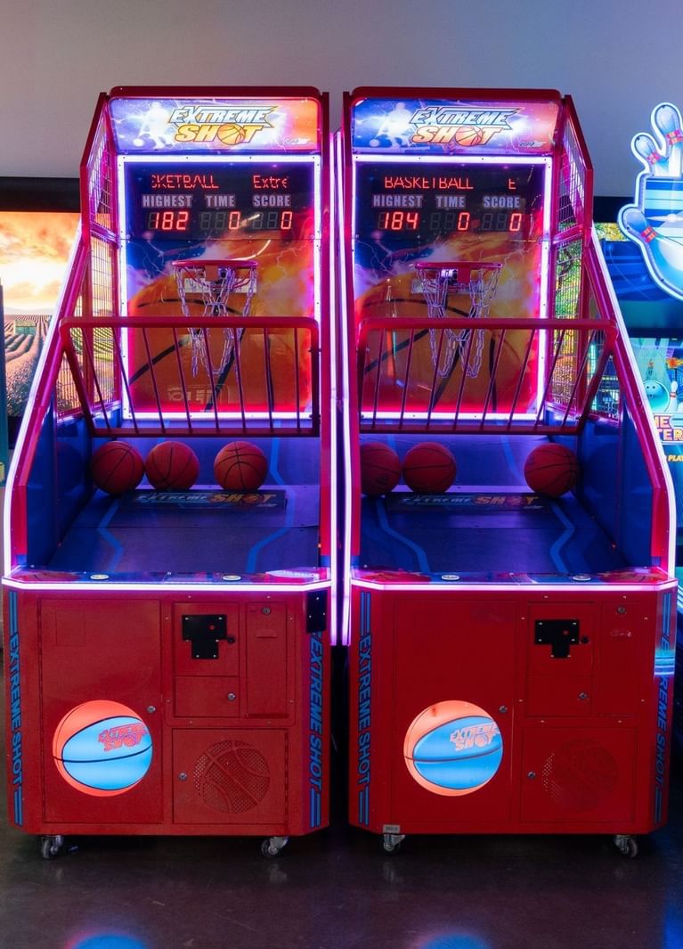 Two red Extreme Shot basketball arcade hoops with balls racked below, under neon trim at Hotel X Toronto