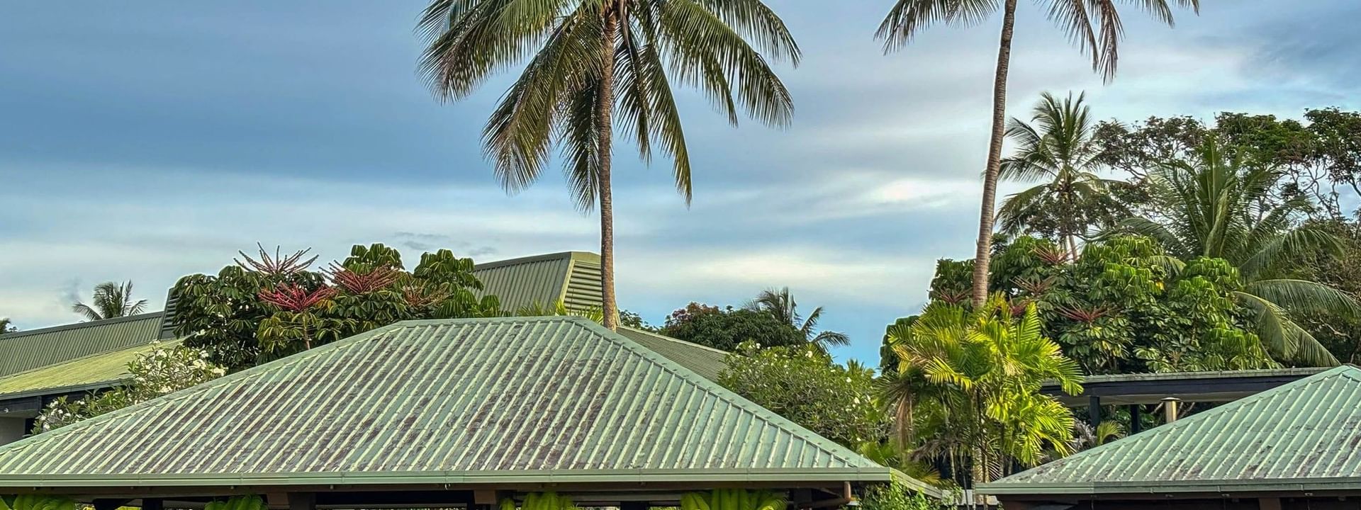 Grill restaurant entrance with Wooden bench on a lawn by a green-roofed pavilion at The Naviti Resort in Korolevu